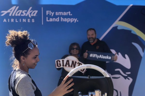 Couple takes photo in front of Alaska airlines branded backdrop at San Francisco Giants baseball game